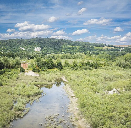 Luftbild Vogelbeobachtungsturm Landschaft mit Fluss, umgeben von Bäumen und Hügeln unter blauem Himmel mit Wolken.
